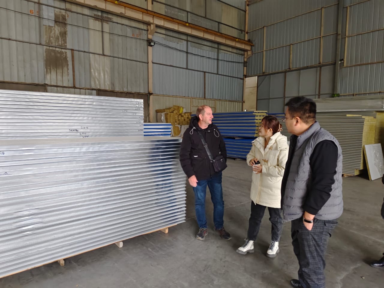 Chris Peo inspecting stacked insulated building panels inside a Chinese factory